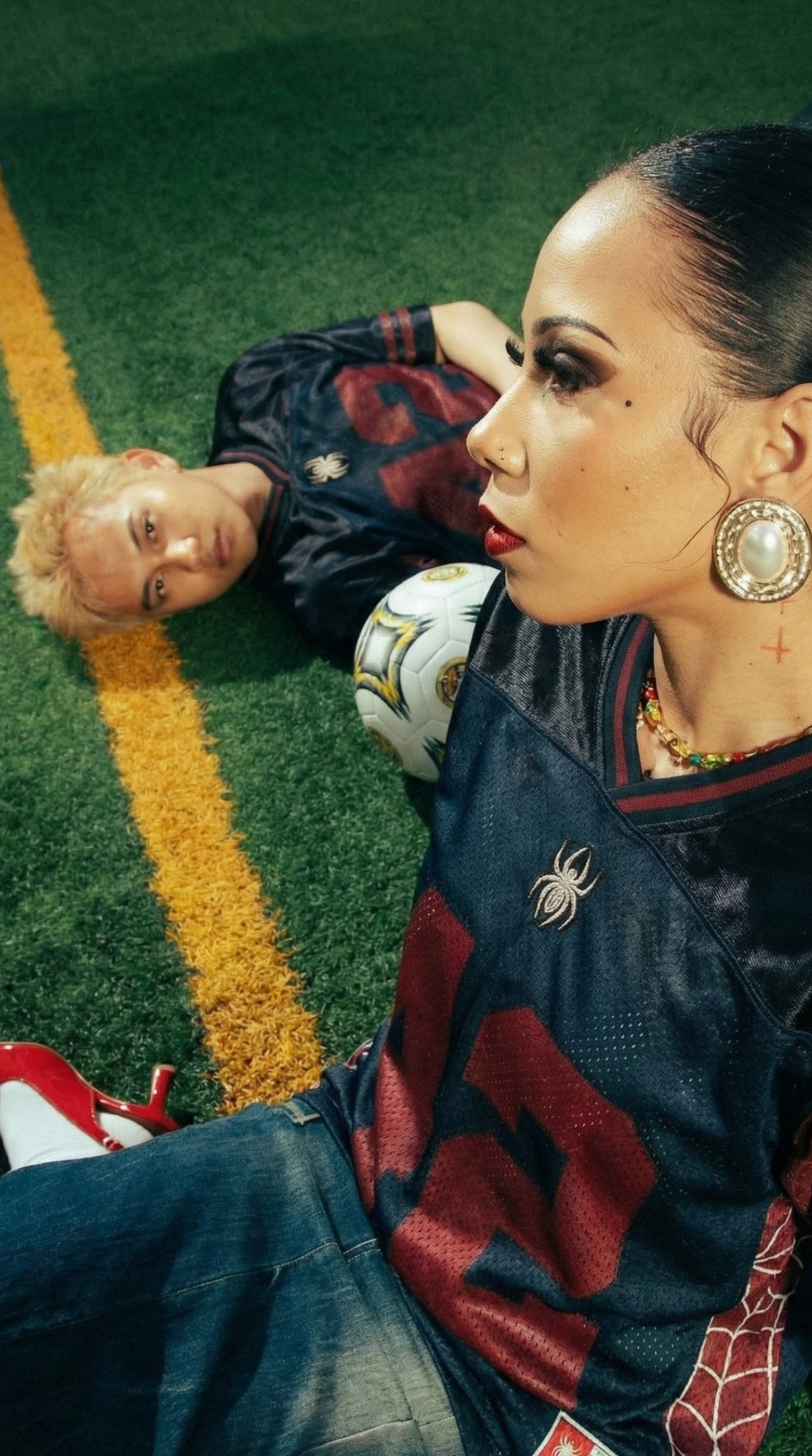 Two people sitting on a grassy field with sports balls.